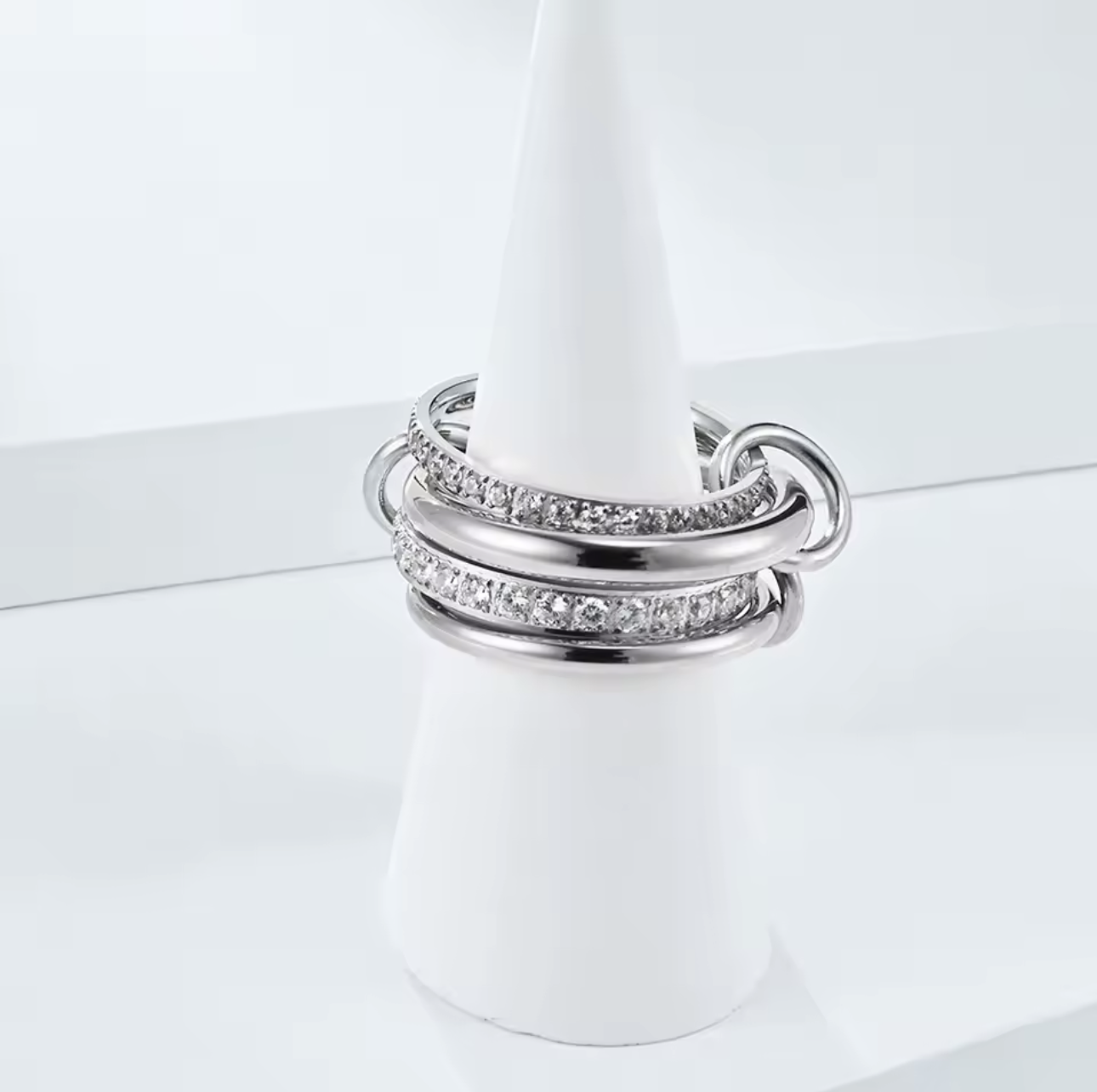 Silver layered link ring, featuring 4 bands - two plan silver and 2 with clear gemstones. Held together by three smaller links pictured on a white background