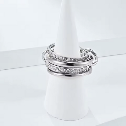 Silver layered link ring, featuring 4 bands - two plan silver and 2 with clear gemstones. Held together by three smaller links pictured on a white background