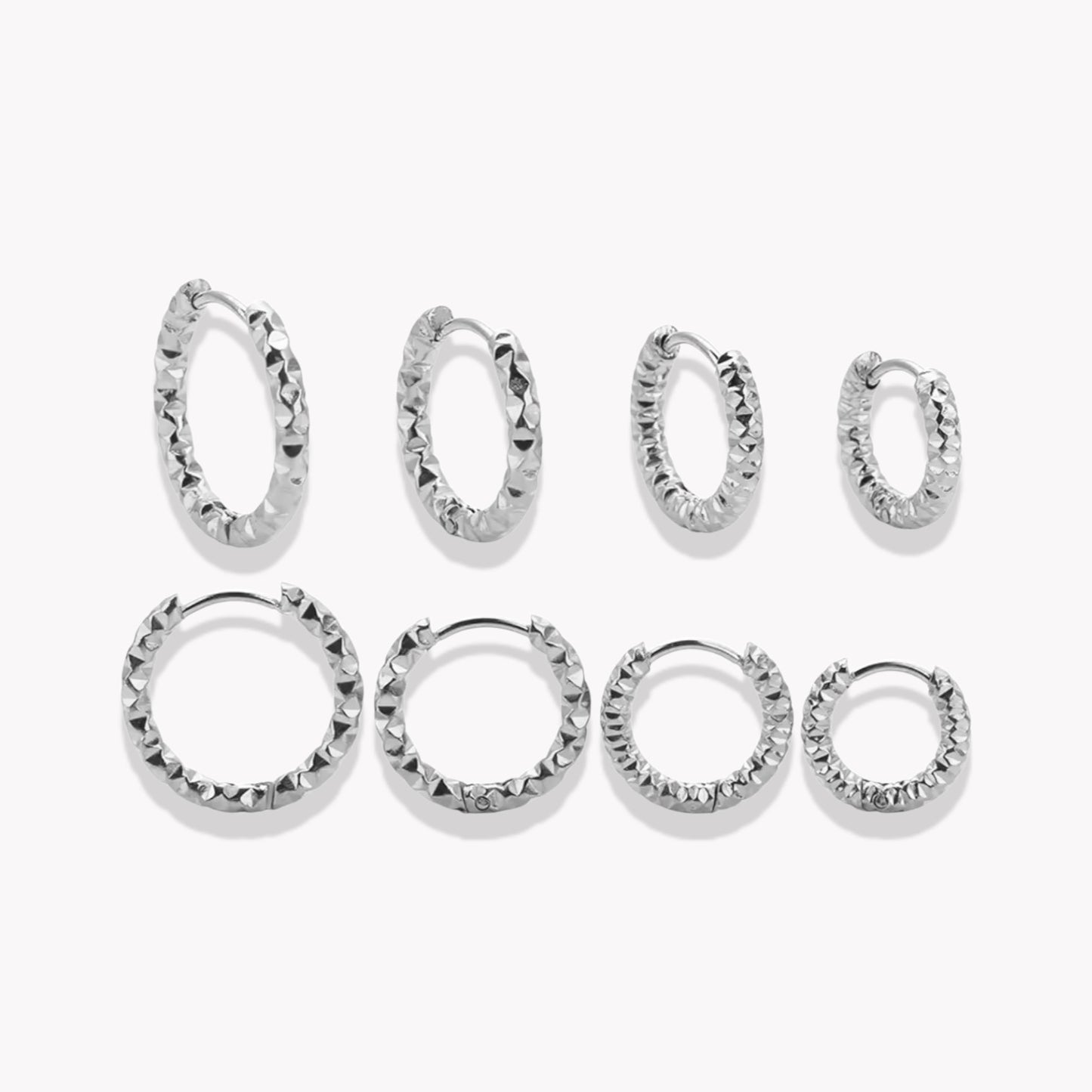 A collection of silver hooped earrings in varying sizes, with a textured design, displayed against a white background.
