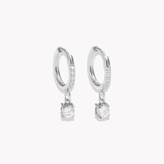 Silver hoop earrings with diamonds on the hoop and a round shaped drop pendant on a white background