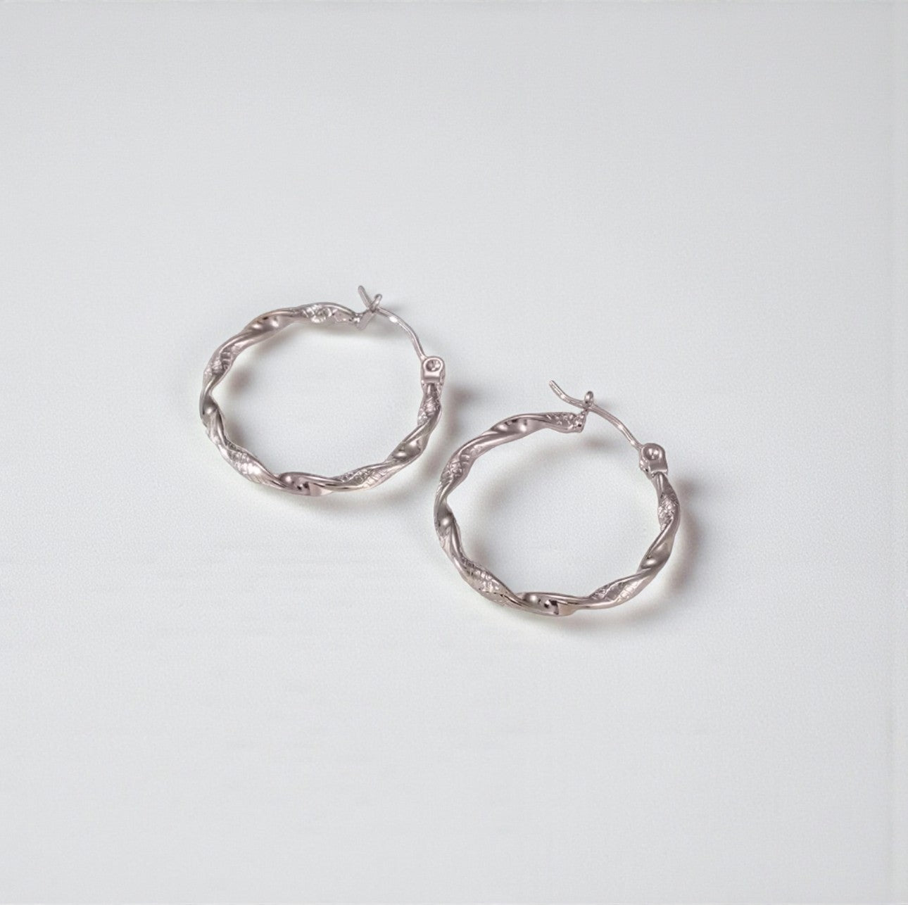 Silver twist hoop earrings on a light gray background