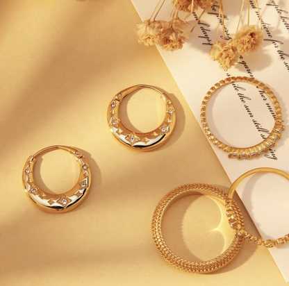 Gold hoop earrings on a yellow surface with dried flowers and text.