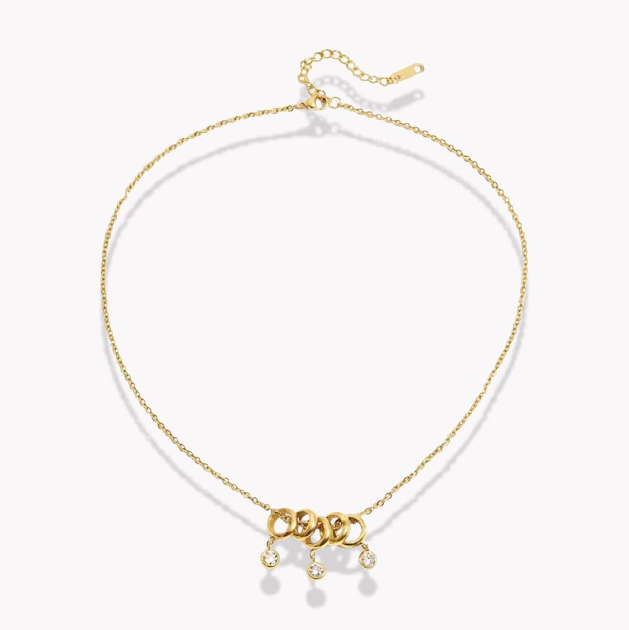 gold necklace with 5 rings that move independently of one another. Three of the rings have drop gemstones dangling from them. Pictured on a white background
