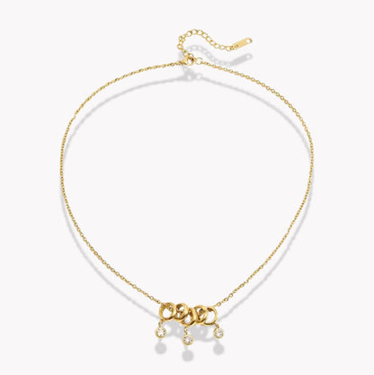 gold necklace with 5 rings that move independently of one another. Three of the rings have drop gemstones dangling from them. Pictured on a white background