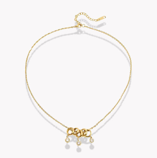gold necklace with 5 rings that move independently of one another. Three of the rings have drop gemstones dangling from them. Pictured on a white background