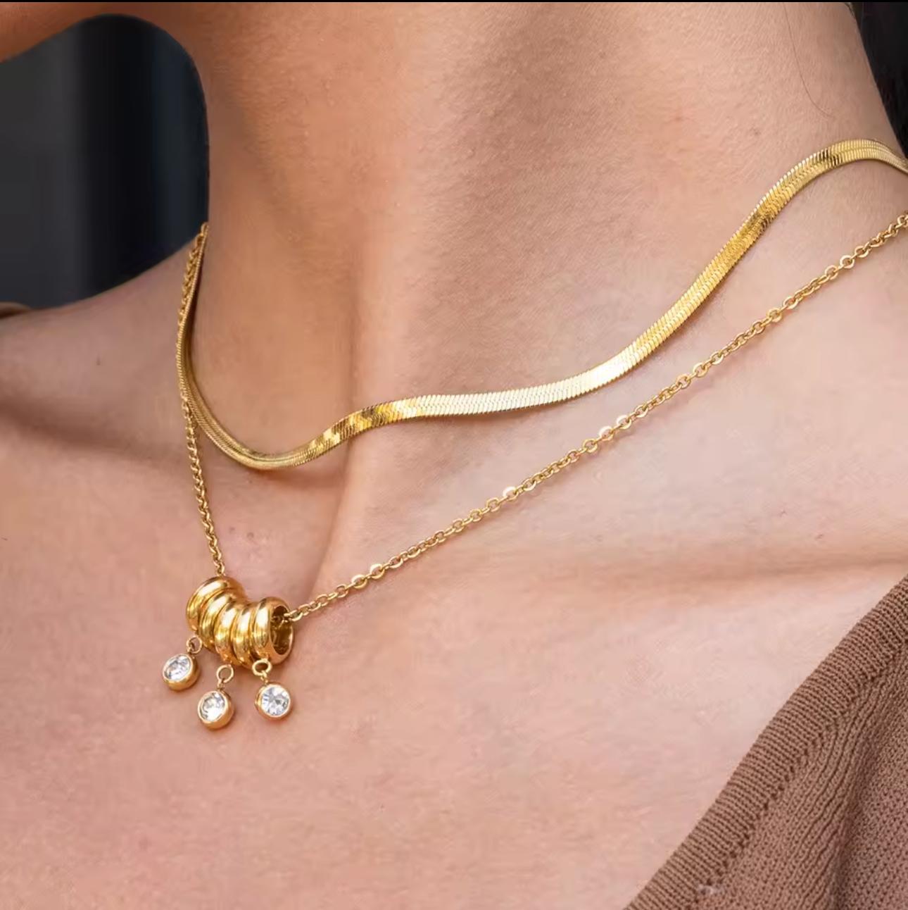 gold necklace with 5 rings that move independently of one another. Three of the rings have drop gemstones dangling from them. Pictured on a neck with another necklace