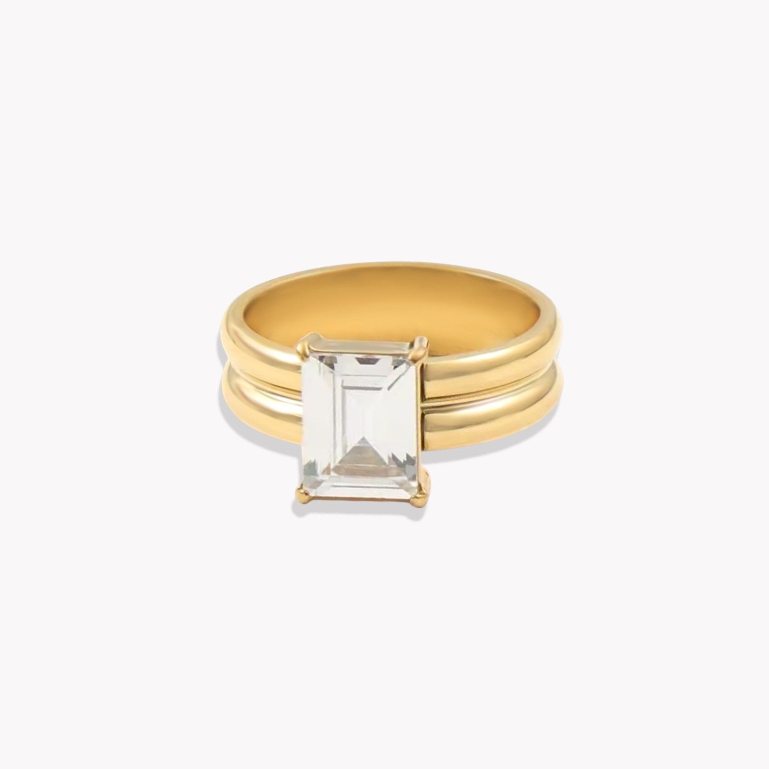 Gold ring with a thicker band and large rectangular gemstone on a white background