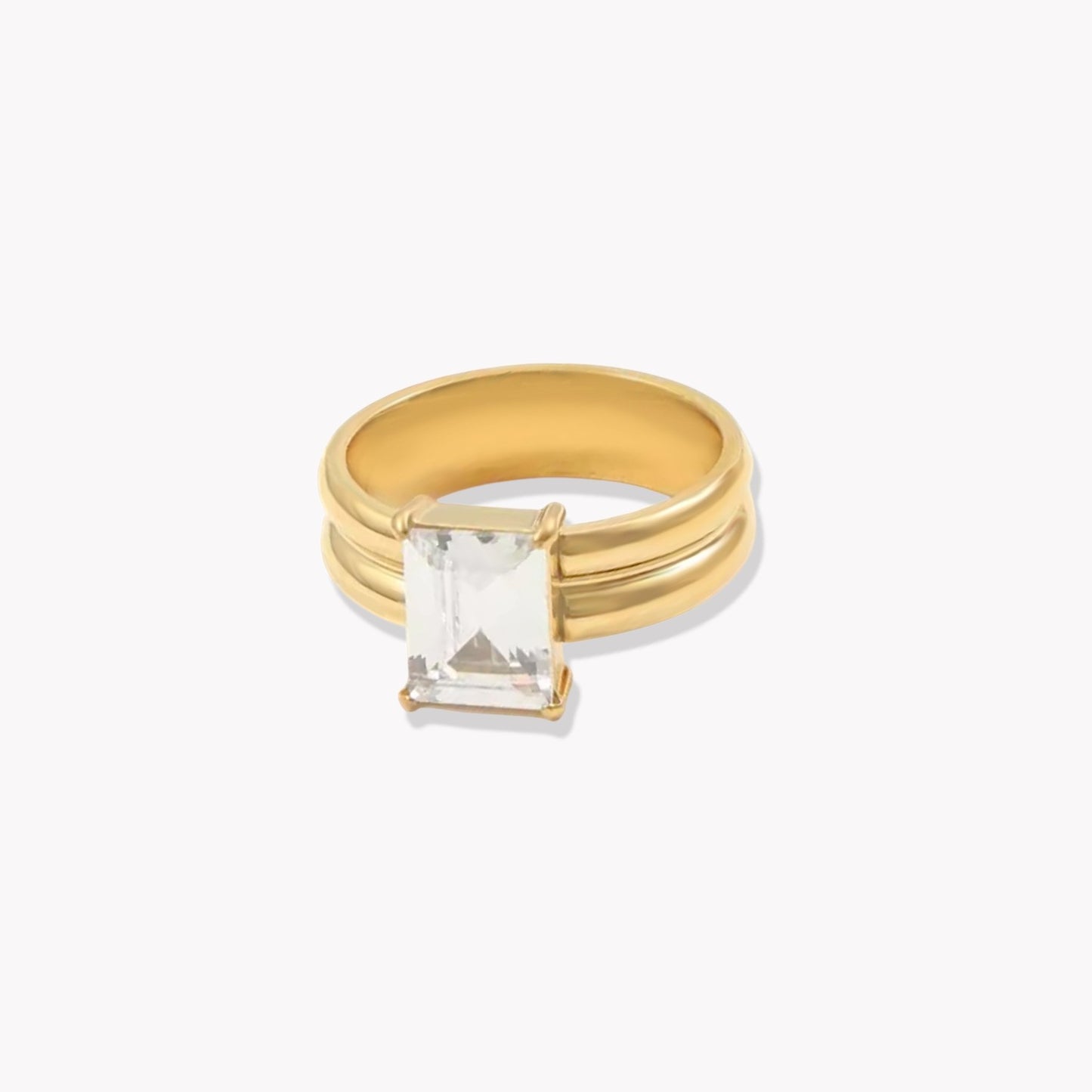 Gold ring with a thicker band and large rectangular gemstone on a white background