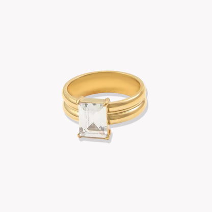 Gold ring with a thicker band and large rectangular gemstone on a white background