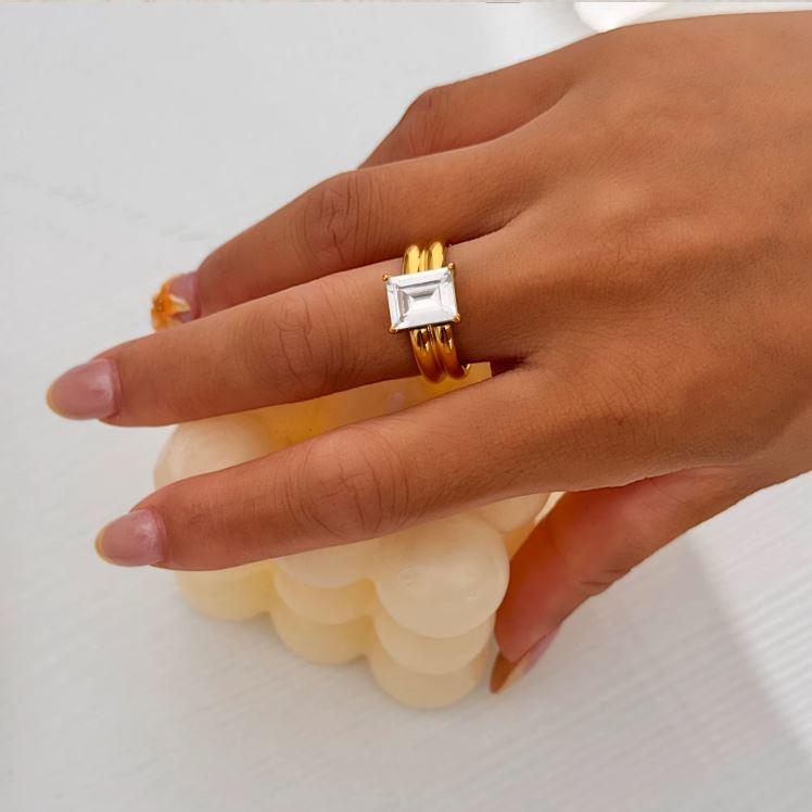 Gold ring with a thicker band and large rectangular gemstone on a finger
