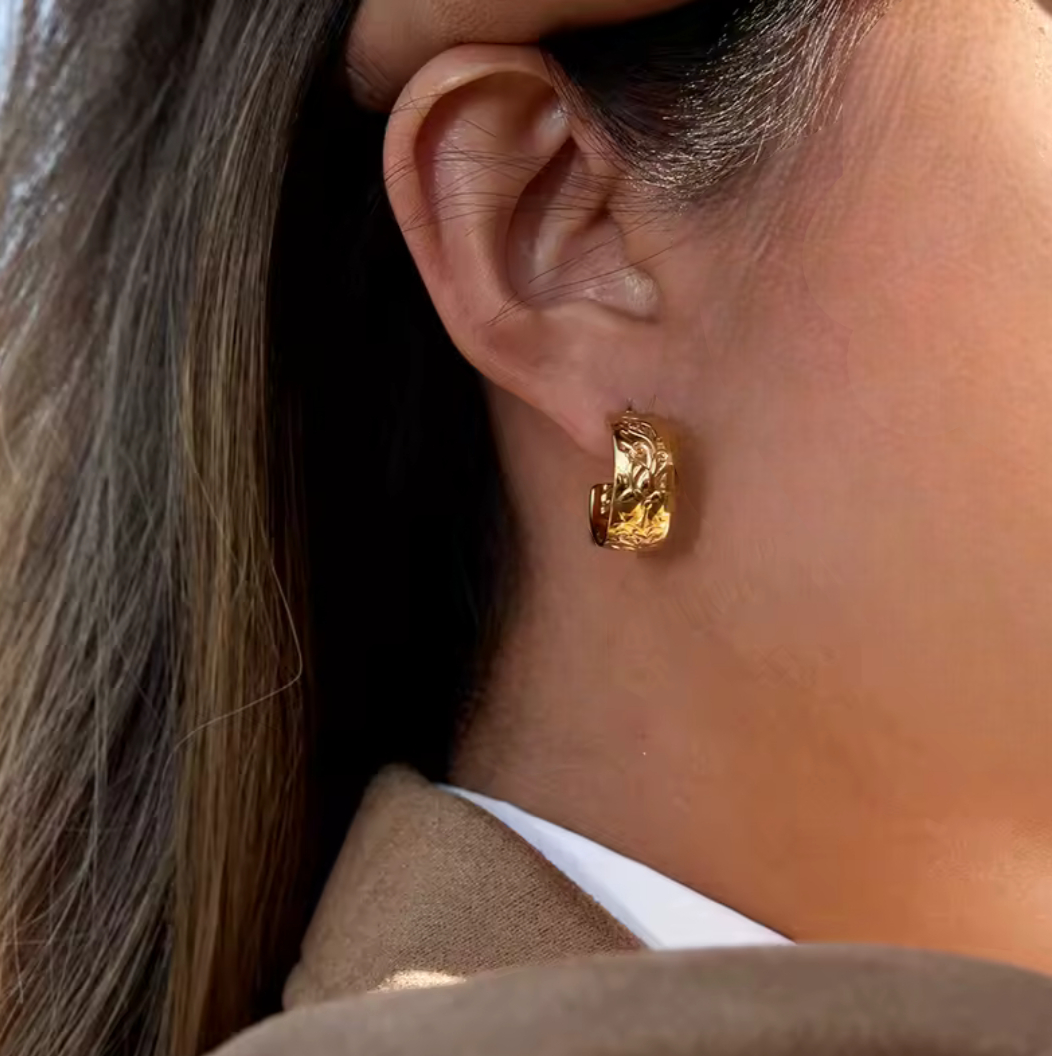 Gold earrings featuring intricate embossed detail being worn in an ear