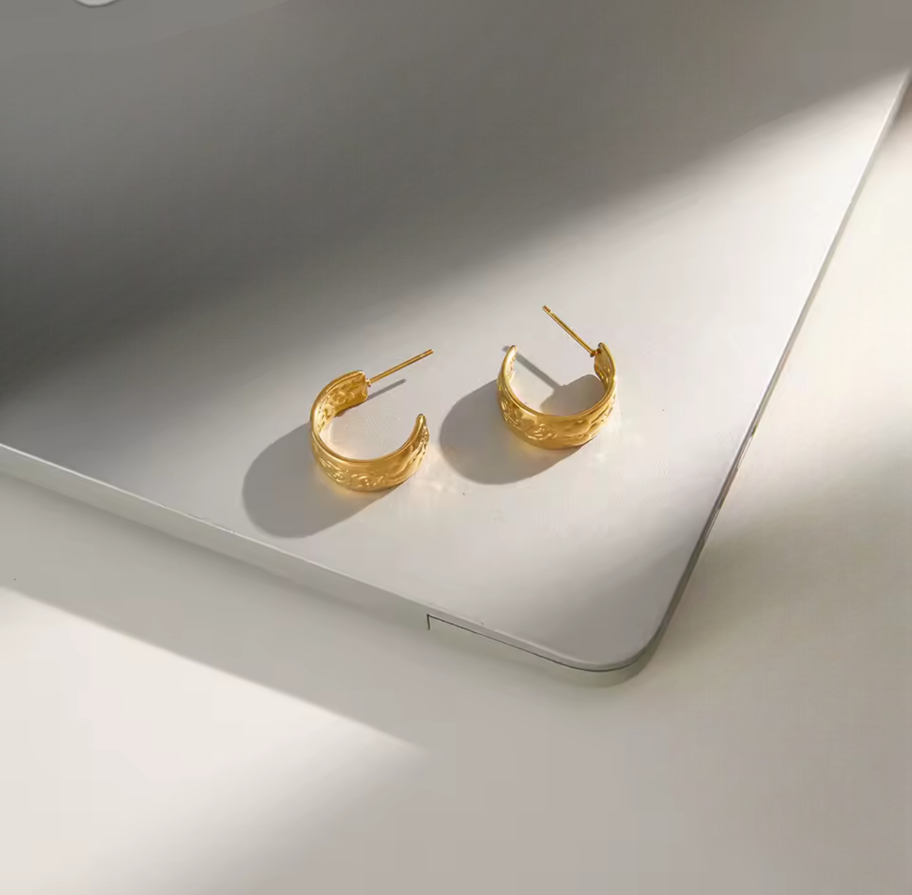 Gold earrings featuring intricate embossed detail pictured on a neutral background