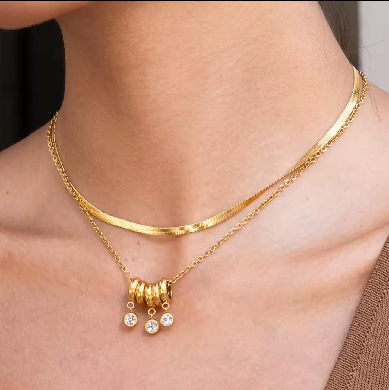 gold necklace with 5 rings that move independently of one another. Three of the rings have drop gemstones dangling from them. Pictured on a neck with another necklace