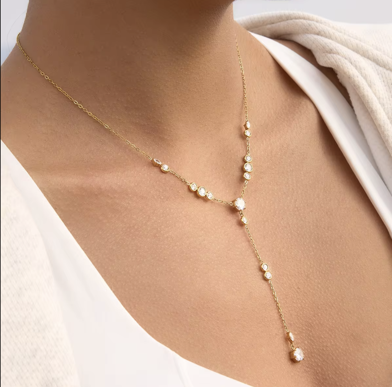 Gold necklace with clear gemstones on a person wearing a white top