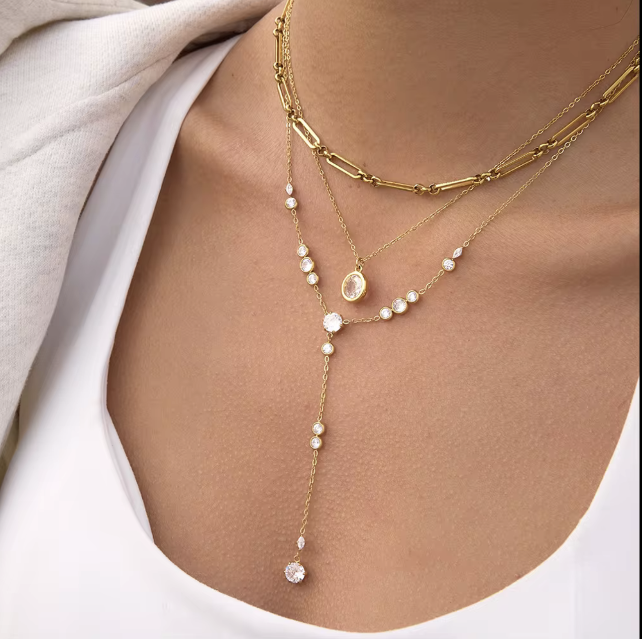 Gold necklace with clear gemstones on a person wearing a white top
