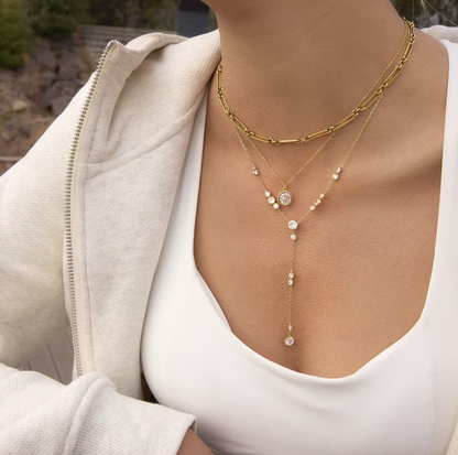 Gold necklace with clear gemstones on a person wearing a white top