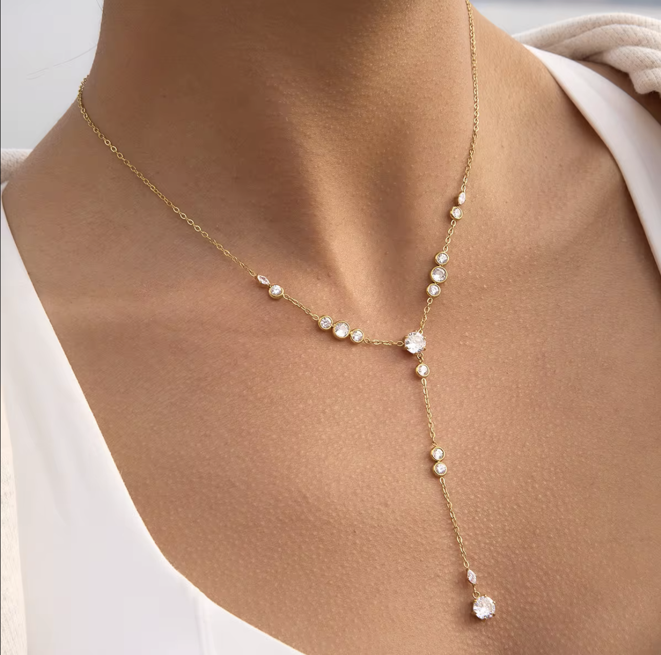 Gold necklace with clear gemstones on a person wearing a white shirt