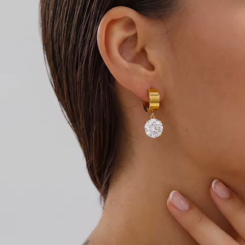 Gold hoop earring with a diamond drop worn by a person on a plain background