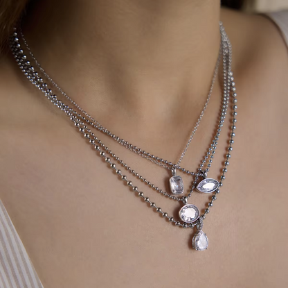 A close-up of a model wearing a multi-layered silver necklace with clear faceted gemstone pendants.