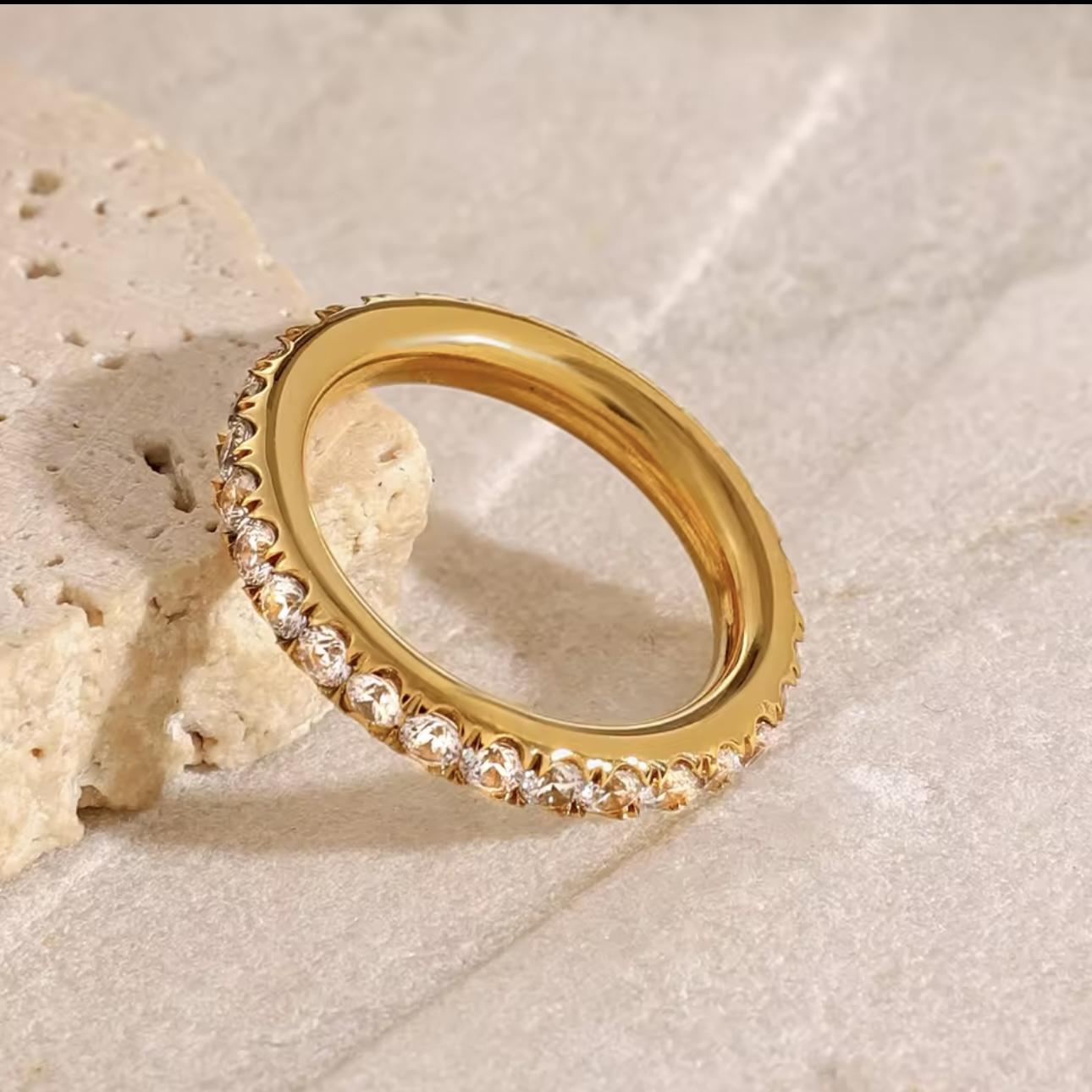 Gold ring with diamond accents on a textured beige surface