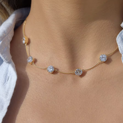 Gold necklace with gemstones on a person's wrist against a blurred natural background