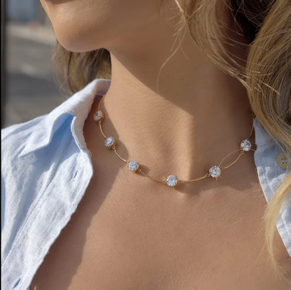 Gold necklace with gemstones on a person's wrist against a blurred natural background
