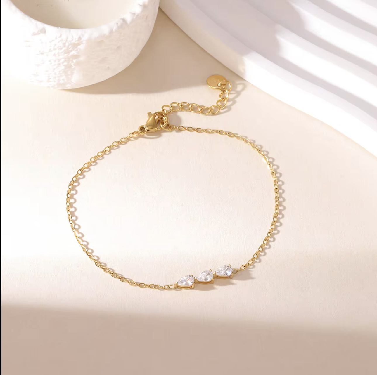 gold dainty bracelet with small pear shaped gemstone detail pictured on a neutral background