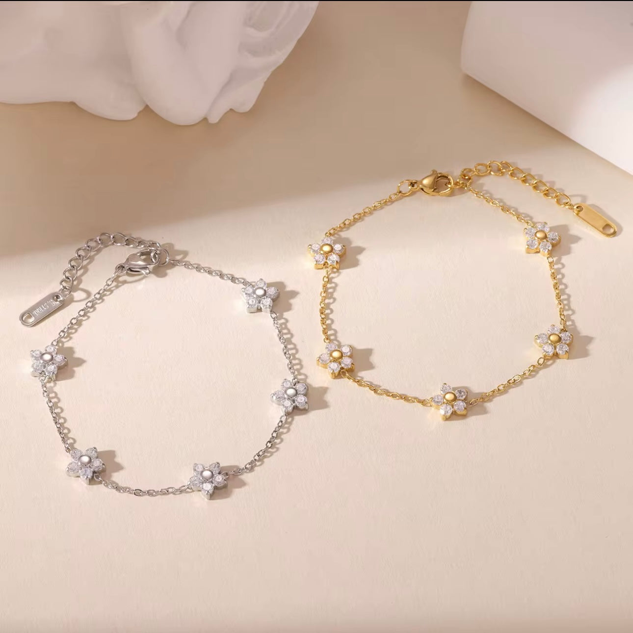 Gold and silver bracelets with clear gemstone floral design on a biege background