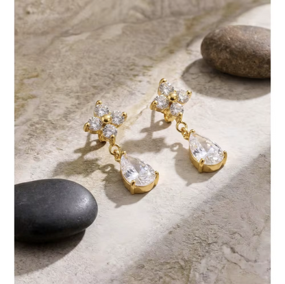 Gold earrings with clear teardrop-shaped gemstones on a stone surface