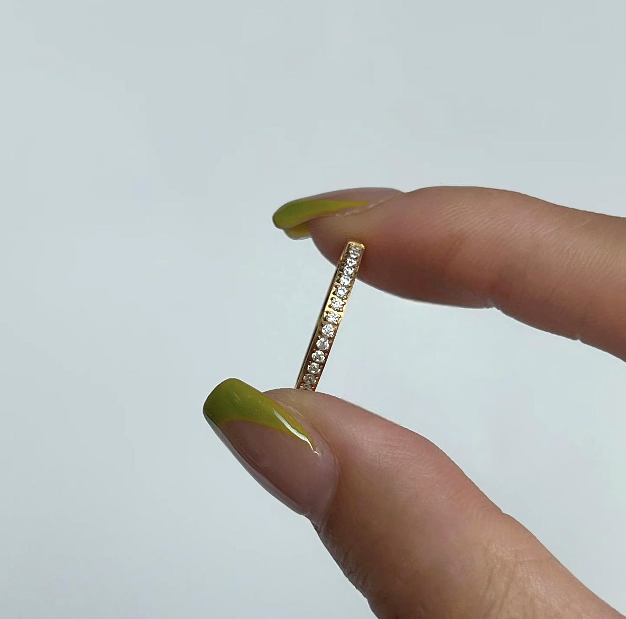 Gold ring with small diamonds held between two fingers against a light gray background