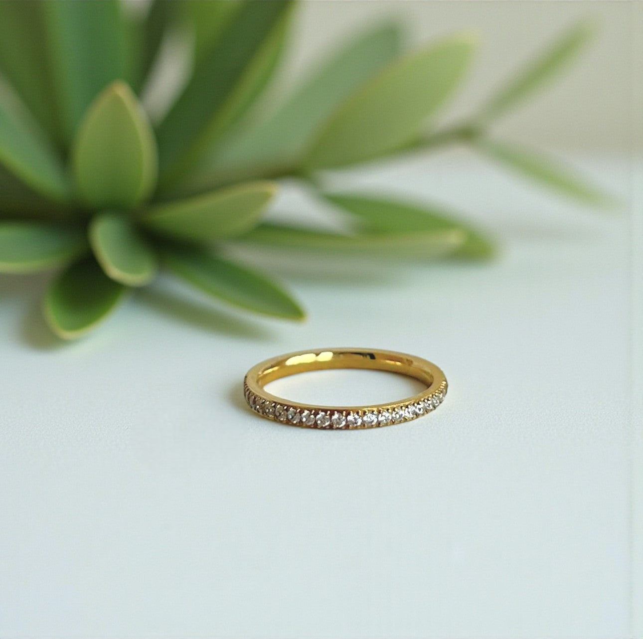 Gold ring with small diamonds on a light green surface with a plant in the background