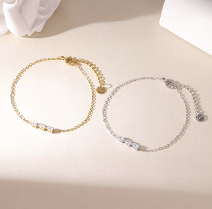 gold and silver dainty bracelets with small pear shaped gemstone detail pictured on a neutral background