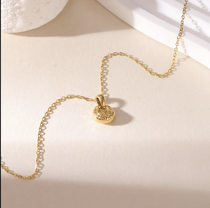 gold necklace featuring small pendant with a textured engave detail pictured on a light background