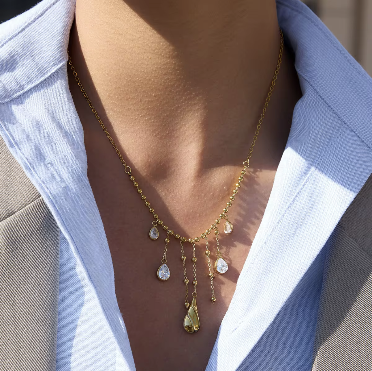 3 gold necklaces layered together. one as a small paperclip necklace, the second is a snake chain and the third is a longer chaing with dangling gemstones. Pictured being worn around the neck