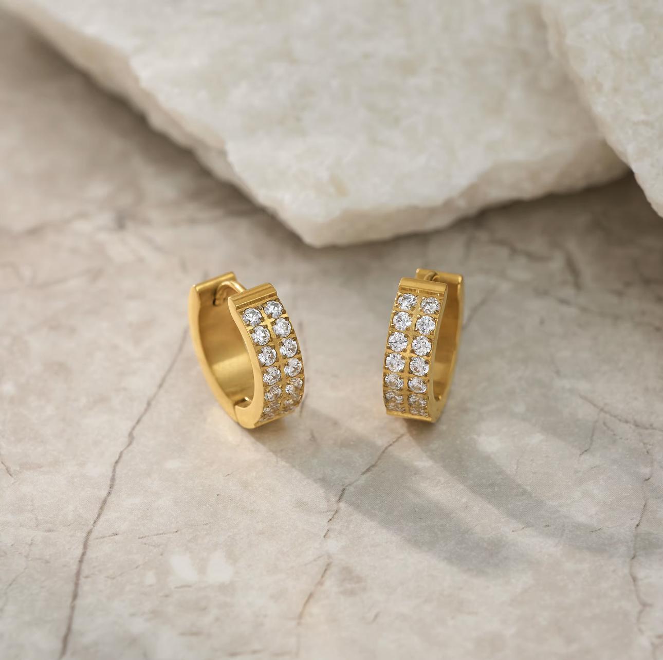 Gold hoop earrings with embedded diamonds on a textured beige surface