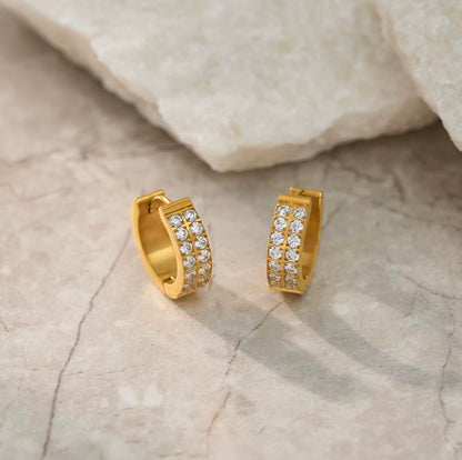 Gold hoop earrings with embedded diamonds on a textured beige surface