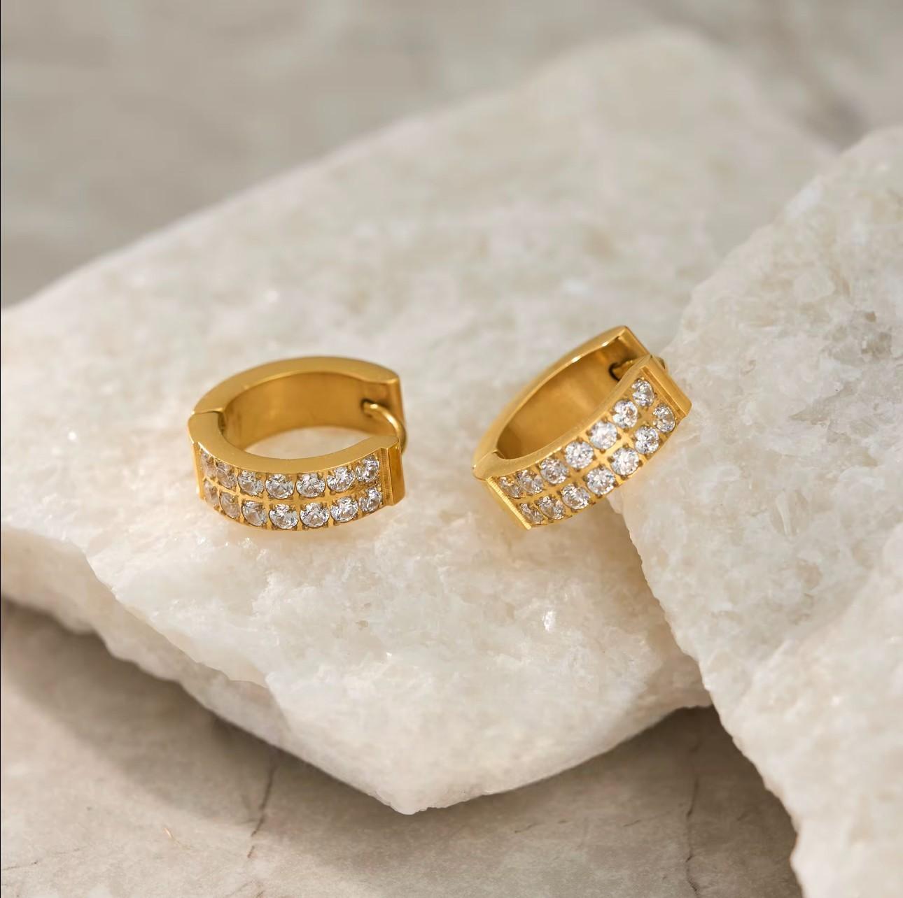 Gold hoop earrings with embedded stones on a textured beige surface