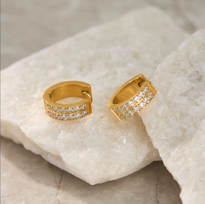 Gold hoop earrings with embedded stones on a textured beige surface