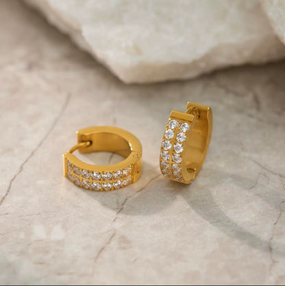 Gold hoop earrings with clear stones on a textured beige surface