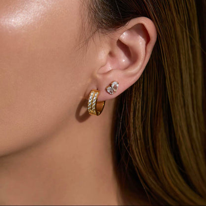 Close-up of a person wearing gold hoop earrings with clear gemstones.
