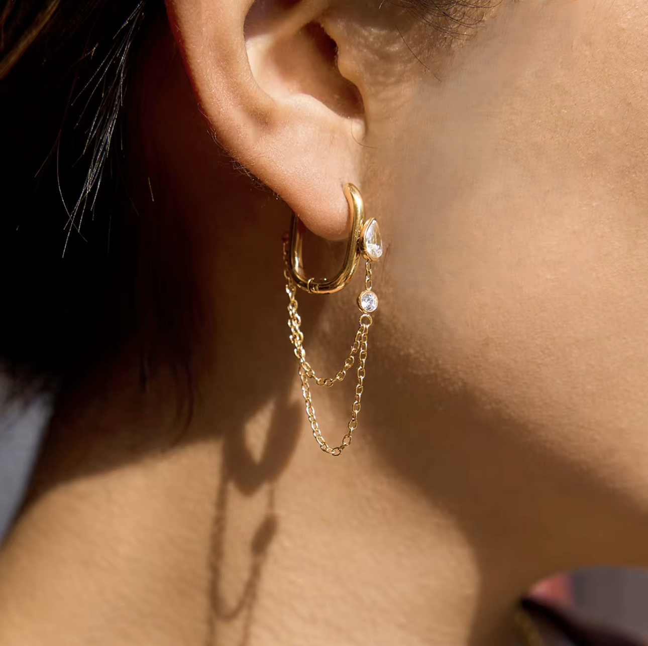 Close-up of an ear wearing a gold hoop earring with chain detail.