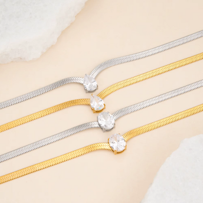 2 silver and 2 gold necklaces with oval and pear gemstones pictured on a light beige background