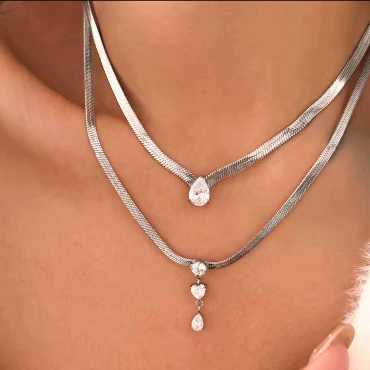 Silver necklace with heart and teardrop pendants on a person's neck