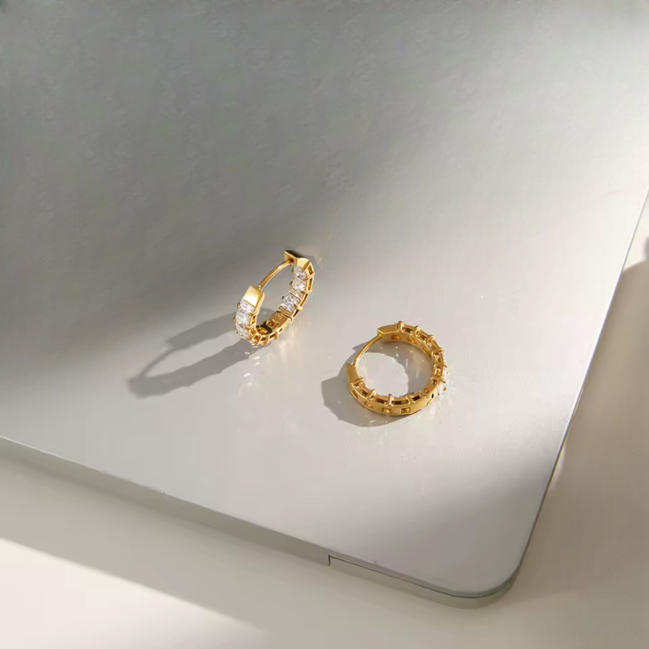 Gold hoops featuring gemstone detail pictured on a light grey background