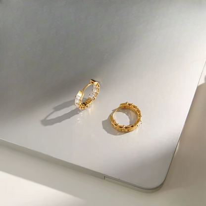 Gold hoops featuring gemstone detail pictured on a light grey background