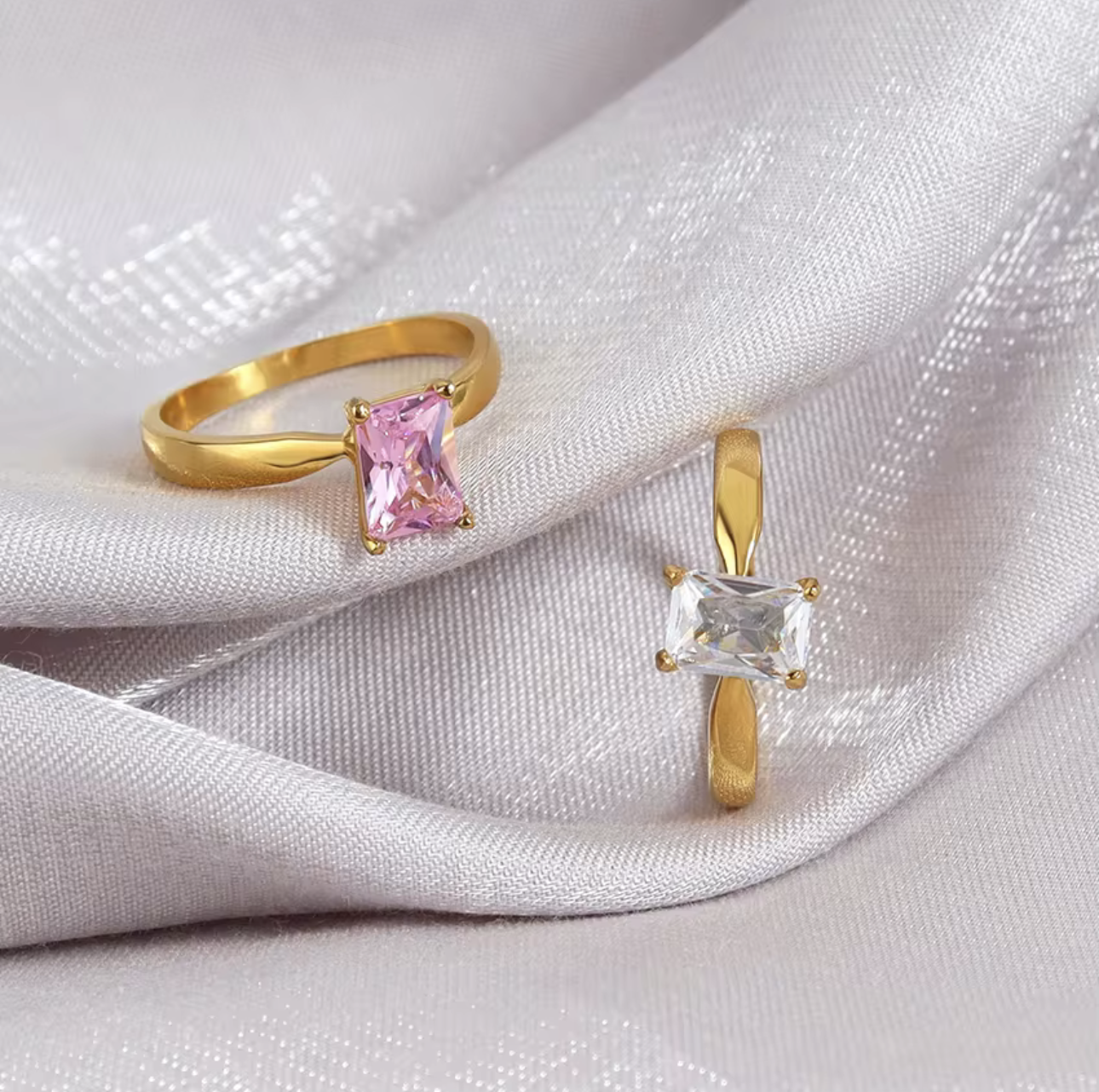 Two gold rings with gemstones on a white fabric background