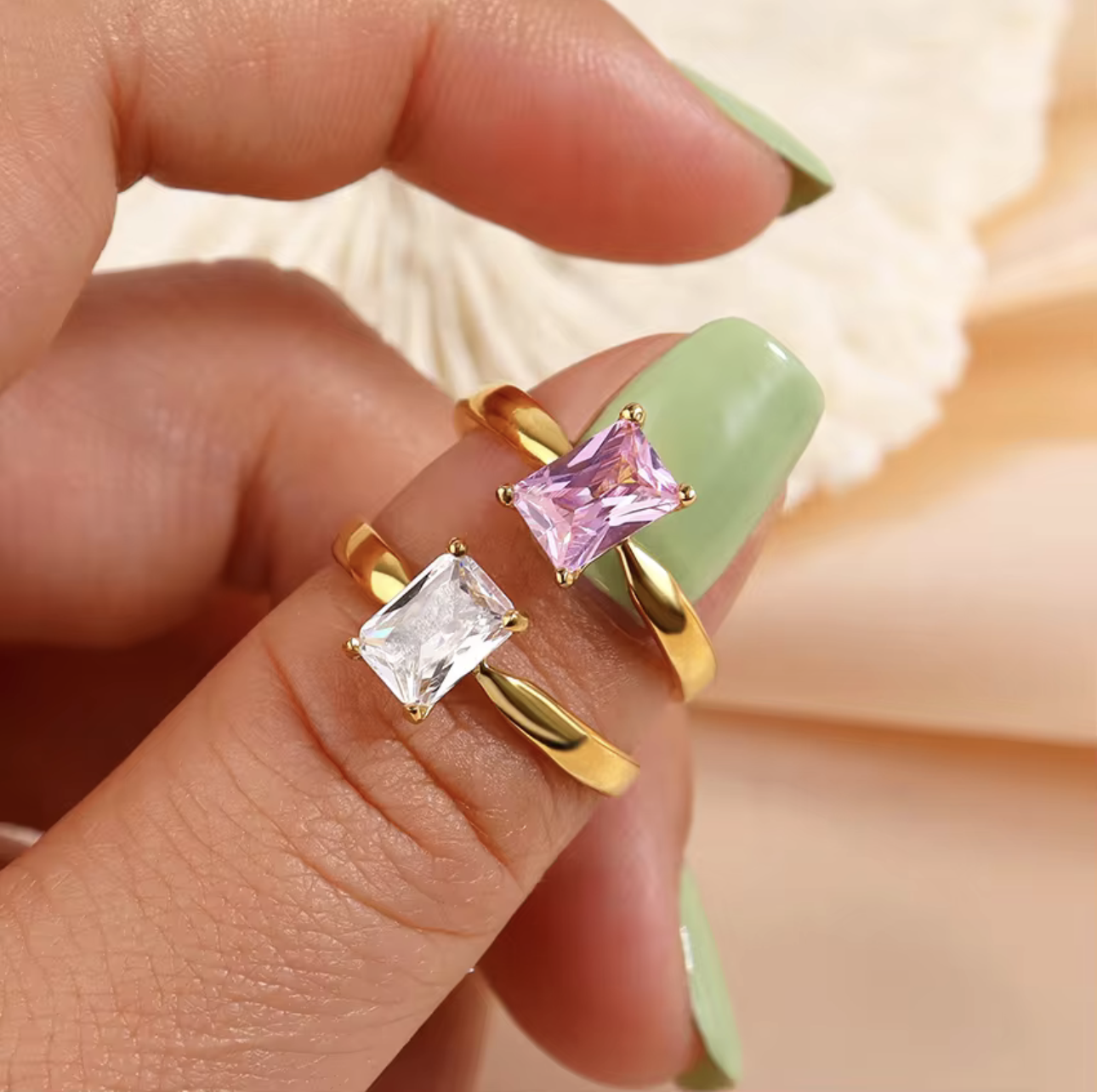 Two rings with square-cut gemstones on a finger against a neutral background