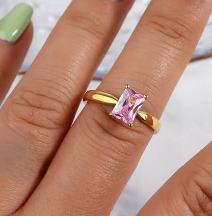 Gold ring with a pink gemstone on a person's finger against a neutral background