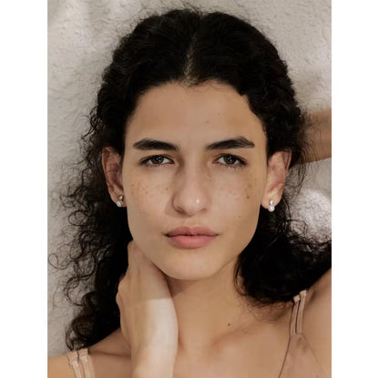 Close-up of a person with dark hair and earrings against a neutral background
