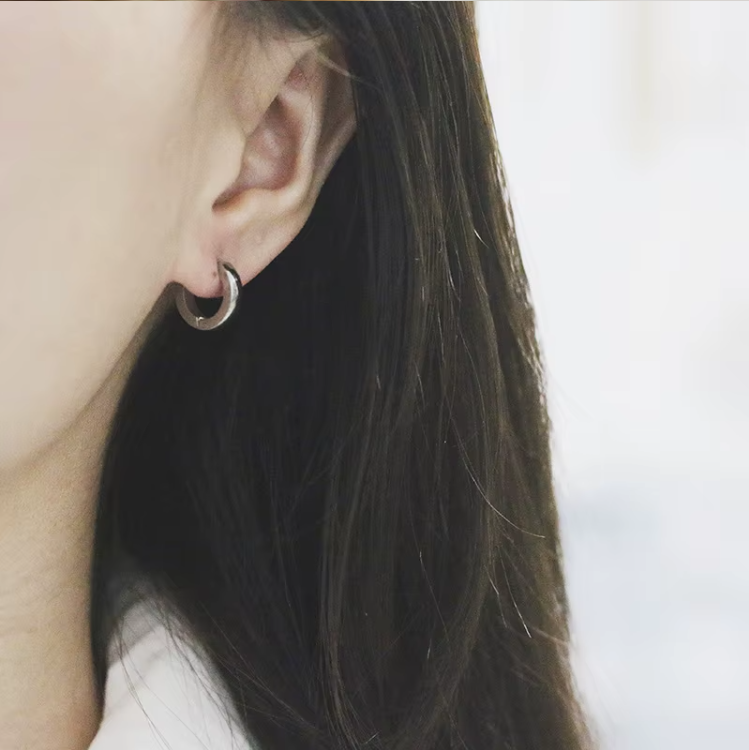 Close-up of an ear wearing a silver hoop earring with blurred background